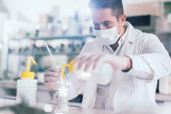 ラボ環境で、科学者がボトルから容器へ慎重に液体を注いでいる