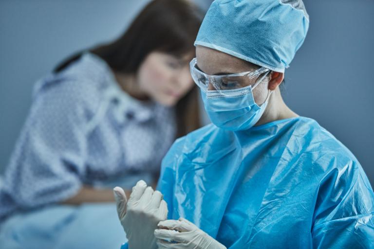 病院のガウンを着た女性患者の前にいる医師が、手術用の服を着用している。