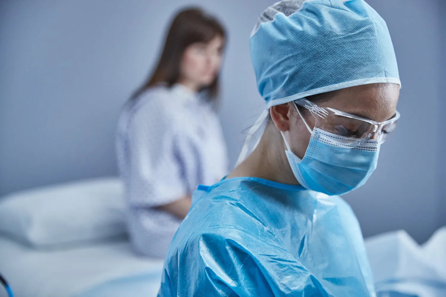 病院のガウンを着た女性患者の前にいる医師が、手術用の服を着用している。